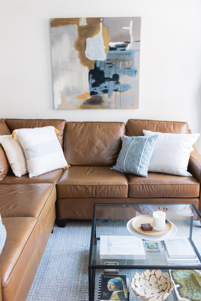 A cozy corner with a leather sectional, layered blankets, and a soft rug surrounded by natural light.